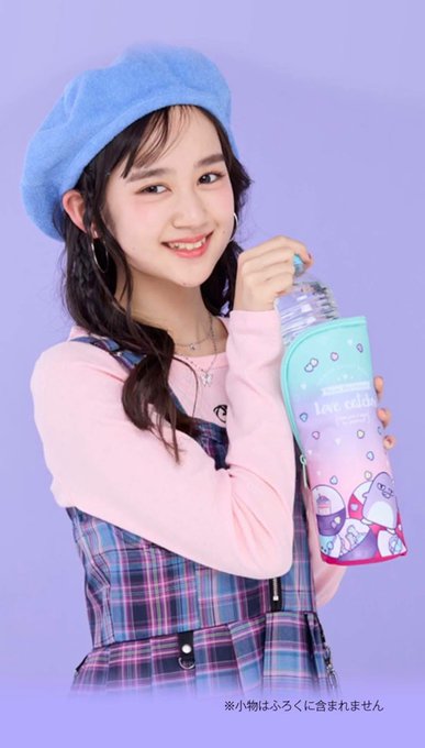 A smiling young woman wearing a blue beret, pink long-sleeve top, and plaid overalls, holding a clear bottle with a pastel purple and blue sleeve that has cartoon characters and the text 'Love Celeb!'.
