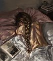 A small, blurry image showing a person partially visible beneath pink and white bedding in a dimly lit room.