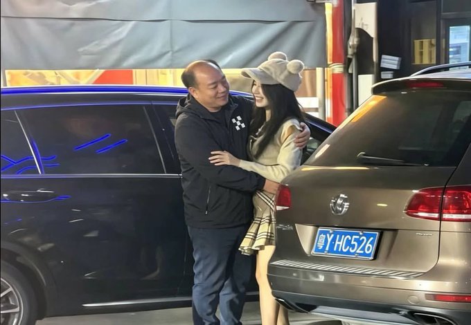 A middle-aged man and a young woman wearing a bear-eared hat share an embrace between two parked SUVs at night, with the license plate "粤Y·HC526" clearly visible on the vehicle behind them. The image accompanies accusations against OKX leadership, appearing to depict one of the alleged incidents referenced in the post about inappropriate workplace behavior.
