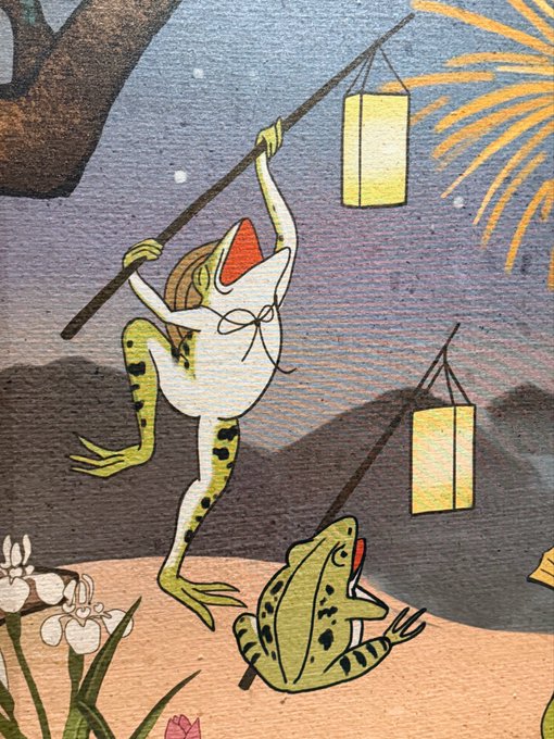 An illustration depicts two frogs in traditional clothing, with one hanging a yellow paper lantern on a pole under a starry sky with fireworks.