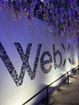 An indoor display features the word 'Web3' made of mosaic tiles on a wall with hanging wisteria flowers and orange line patterns.