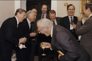 A group of men in suits, including Mikhail Gorbachev and Ronald Reagan, share a laugh with wine glasses at a formal gathering.