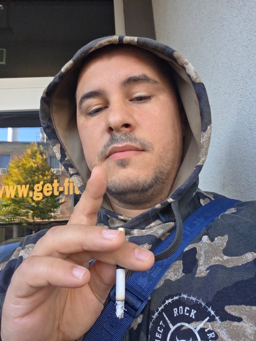 A man wearing a camouflage hoodie with his eyes closed, holding up a finger, with text 'www.get-fit.' partially visible on the left.