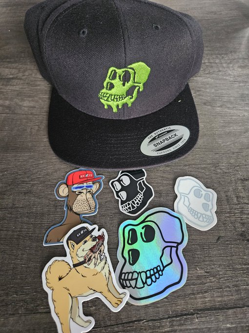 The image features a collection of stickers, including one with a skull design, placed on a wooden surface. The stickers are arranged in various positions, creating an interesting visual effect. The text "Thank you @KaijuTheApe from the @BoredApeYC ptp store!!! Dope asf" is also present in the image, likely indicating that these stickers were purchased at the store and are being shared on social media platforms to promote a brand or product.