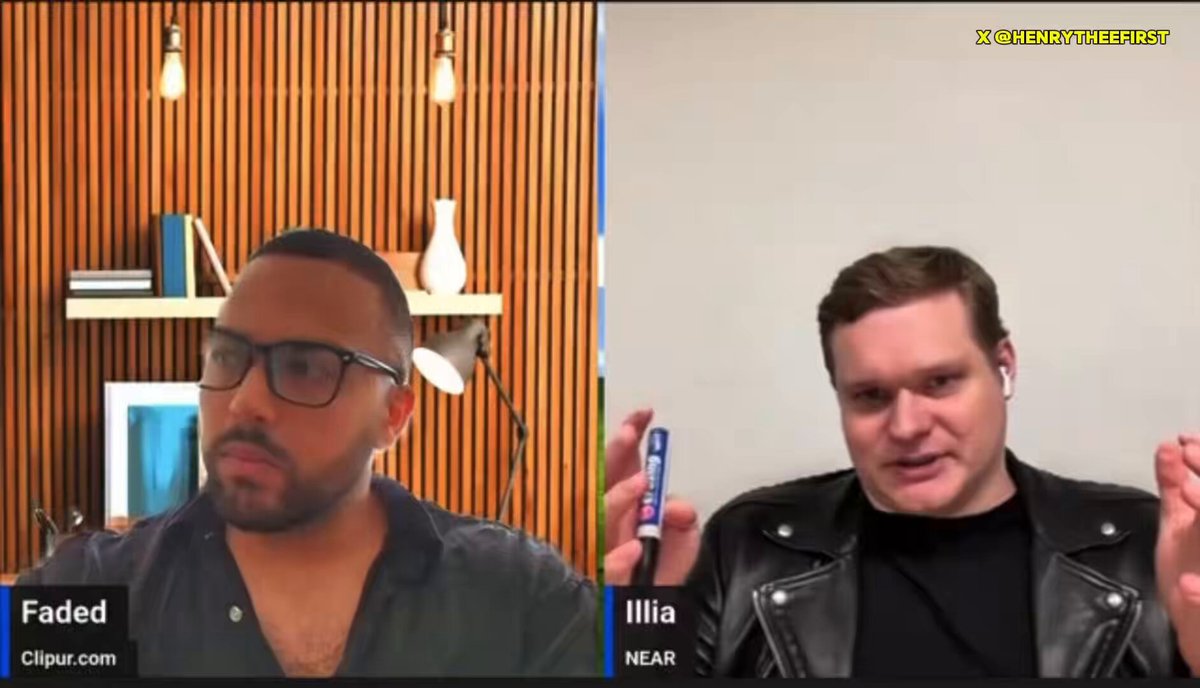 The image shows two men having a conversation over a video call. One man is wearing glasses and a black shirt, while the other has a leather jacket on. They are both looking at each other as they speak. The background of the image features a wooden wall with several books placed on it.