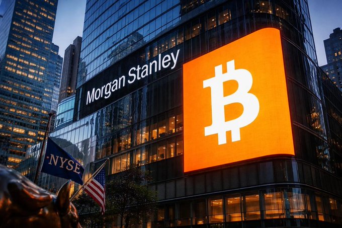 The Morgan Stanley building at night with a large illuminated Bitcoin logo on its facade, alongside an NYSE flag and a bull statue in the foreground.