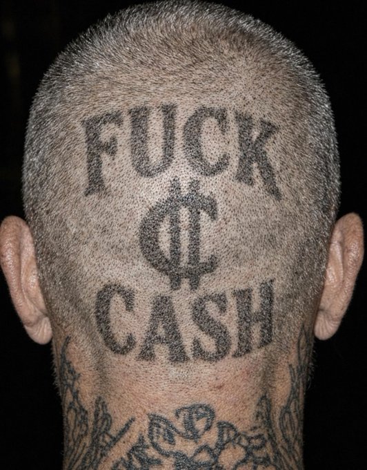 Close-up of the back of a shaved head with a tattoo reading 'FUCK CASH' with a dollar sign between the words.