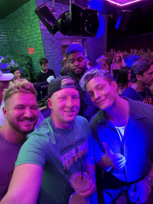 The image shows a group of people standing together, with one man holding a drink in his hand. The background appears to be a dark room or club setting, which could suggest that they are at a party or social event. There are several other people present in the scene as well, indicating a lively atmosphere. The post includes various text elements such as "@doginaldogs @barkmeta @GodsBurnt @Shieldmetax". This might be related to the image's context or could be part of an unrelated conversation happening among the group of friends.

The main focus of the image is on the man holding a drink, which adds a sense of camaraderie and enjoyment to the scene. The presence of other people in the background further emphasizes the social aspect of the gathering. Overall, the image captures a moment of connection and shared experiences among the group members.