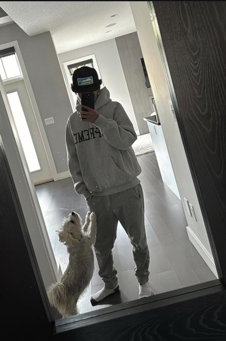 A mirror selfie showing a person in a gray "PRIVÉ" hoodie and black cap, with a small white dog standing on its hind legs against their leg, capturing a casual at-home moment that complements the post's laid-back, networking-focused tone. The bathroom setting and relaxed pose suggest an approachable, personal vibe fitting for someone seeking new connections in web3.