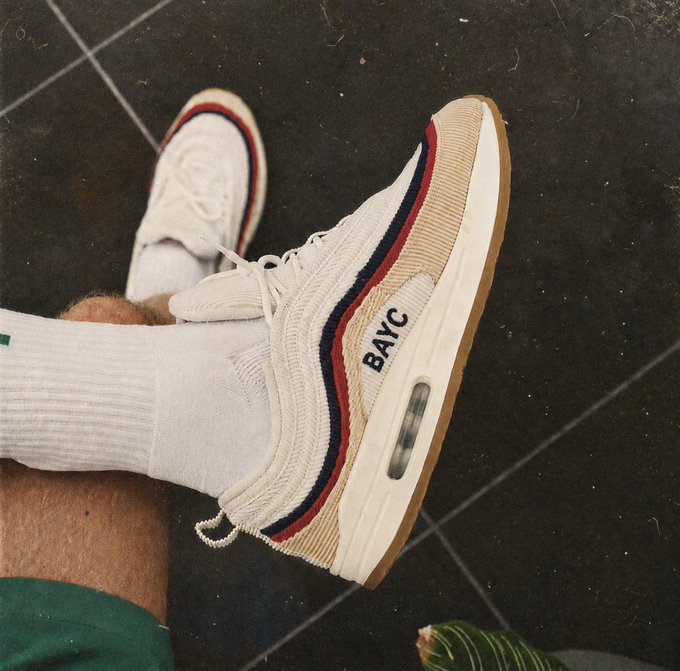 A pair of white and tan Nike Air Max sneakers with red and blue accents, customized with 'BAYC' on the side, worn with white socks.