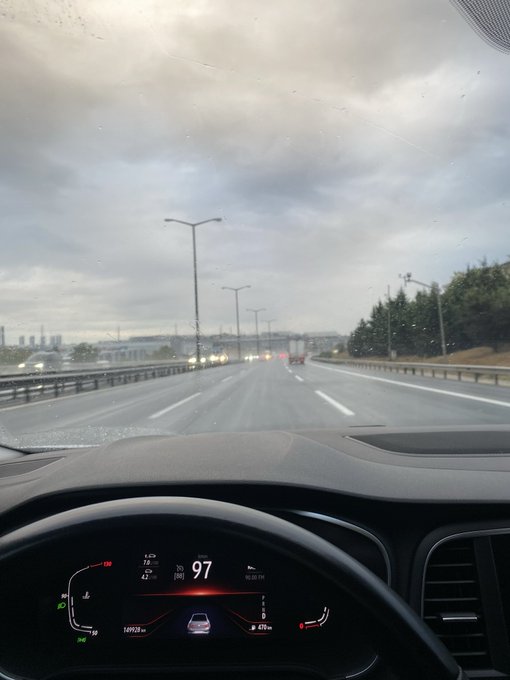 View from inside a car driving on a wet highway under cloudy skies, with the digital dashboard displaying a speed of 97 km/h and 471 km of range remaining.
