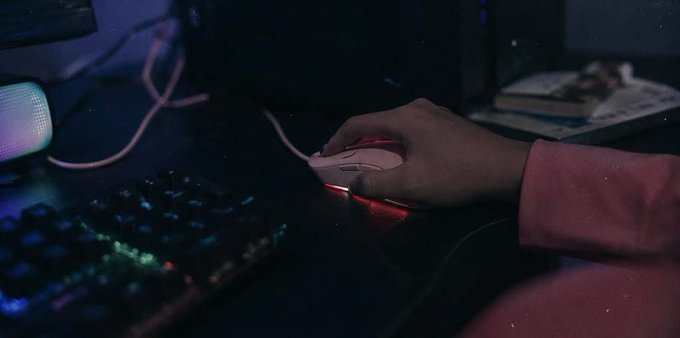 The image shows a person's hand holding a white computer mouse with red lights underneath it. The scene takes place at night, as indicated by the dark background. There are no other people or objects visible in the image, making it an interesting and unique composition that captures the viewer's attention.