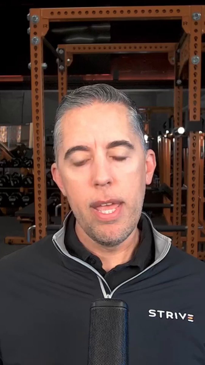 The image features a man wearing a black shirt with white lettering that says "Strive" on his chest. He appears to be talking into a microphone, possibly discussing Bitcoin or related topics. The background of the image shows an indoor setting with several racks of weights and other exercise equipment visible behind him.