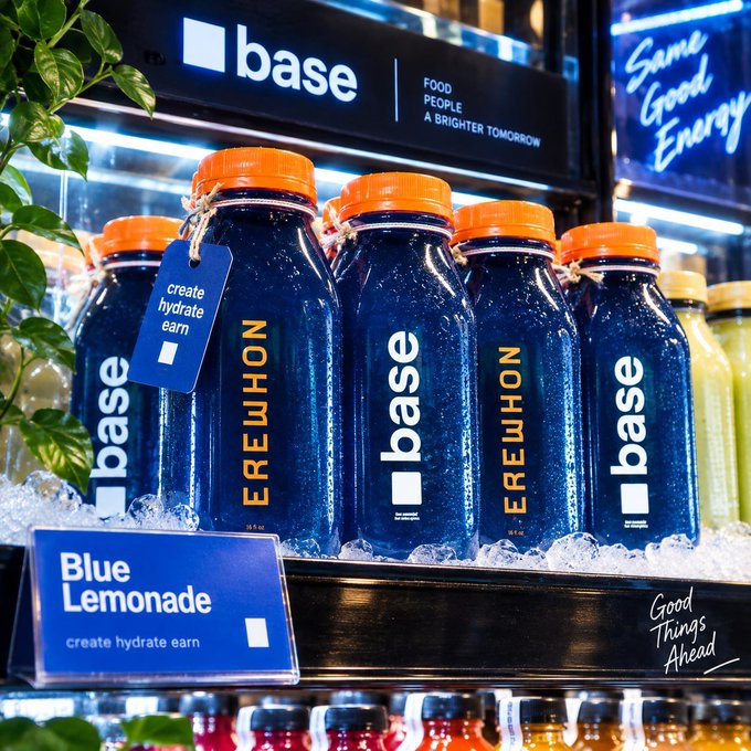 A refrigerated shelf displaying blue 'base' brand beverage bottles with orange caps, labeled as 'Blue Lemonade' with the tagline 'create hydrate earn' and 'Good People A Brighter Tomorrow'.