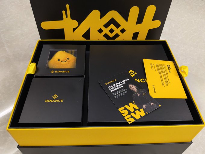 An open Binance gift box with yellow and black branding, containing a plush toy character, branded merchandise, and a promotional card for a "ZVA Global ZWAG Preseason Campaign."