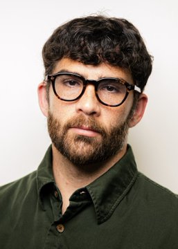 A man with dark curly hair, a beard, and black-framed glasses wears an olive green button-up shirt against a plain white background, likely a headshot of James Talarico, the Texas politician mentioned in the post.