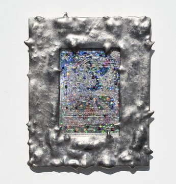 A framed artwork with a textured silver border featuring small spikes, containing a glittery, abstract pixelated design with blue, green, and purple colors.