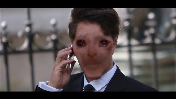 A still image from a video showing a person in a black suit talking on a phone, with their face severely distorted by an AI face-swapping filter.