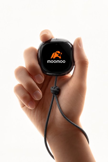 A close-up of a hand holding a small black smartwatch displaying the orange "moomoo" logo on its screen, with a black braided lanyard attached.