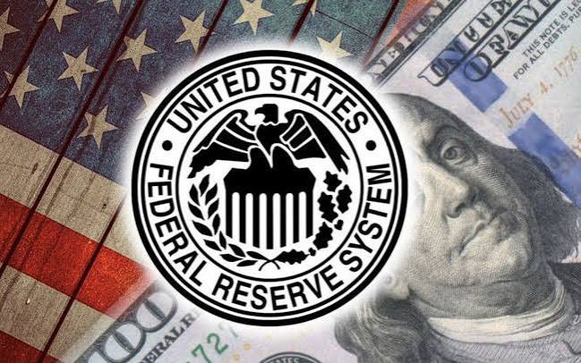 The United States Federal Reserve System seal superimposed over a background of an American flag and a one hundred dollar bill featuring Benjamin Franklin.