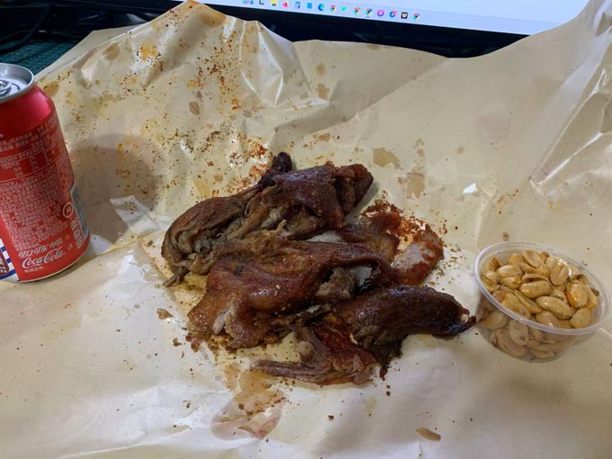A meal of barbecued or roasted meat pieces served on brown butcher paper, accompanied by a Coca-Cola can and a small cup of peanuts.
