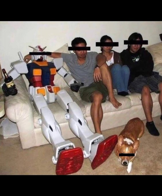 Three young people sitting on a couch next to a life-size Gundam robot model, with a basset hound on the floor in front of them and a beer bottle nearby.