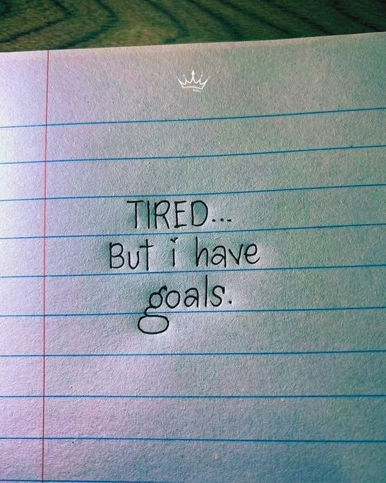 A handwritten note on lined paper featuring a small crown drawing, reading 'TIRED... But i have goals.'