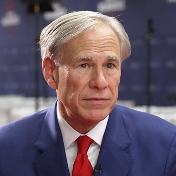 A photograph of an older man with gray hair wearing a blue suit and red tie, appearing on what looks like a news broadcast.