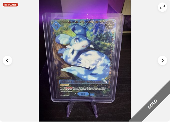 A photograph of a holographic trading card featuring a blue dragon-like creature, displayed in a protective case on a stand and marked with an "IN 1 CART" badge and "SOLD" label.