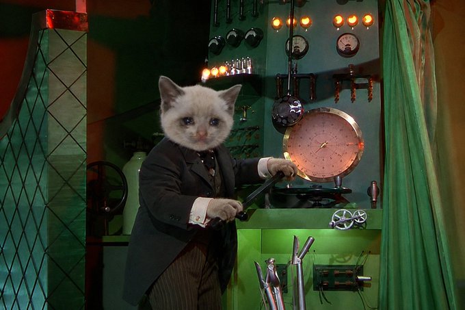 A cat with a human body wearing a formal suit and operating machinery in a vintage, steampunk-style room.