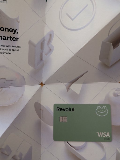 A green Revolut Visa Infinite debit card rests on a tiled surface with partial text reading "money, smarter" and "with features...intelligence to spend...more smarter." The image ties to the post's claim that even Revolut has been "coded" by Tibbir, with the card and slogan serving as playful visual proof.
