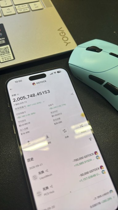 A smartphone displays the GSTOCK trading app showing a portfolio of 2,005,748.45153 GSTOCK tokens (approximately $40,525.72), with recent transactions including a +700,000 GSTOCK purchase and a -50,000 GSTOCK sale, photographed next to a Yoga laptop and a mint-green mouse on a desk.
