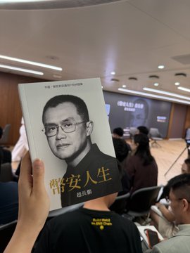 A hand holds up a book titled 'CHRIS WANG' featuring a portrait of a man on the cover, at what appears to be a public event or seminar.