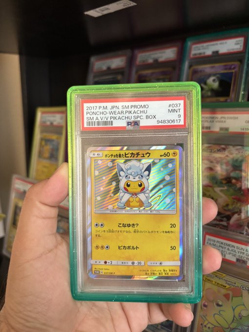 A hand holding a PSA-graded 2017 Japanese Pokémon card, 'Poncho-Wearing Pikachu SM-A V.V.V WearPikachu SPC_BOX,' graded MINT 9, in a green protective case.