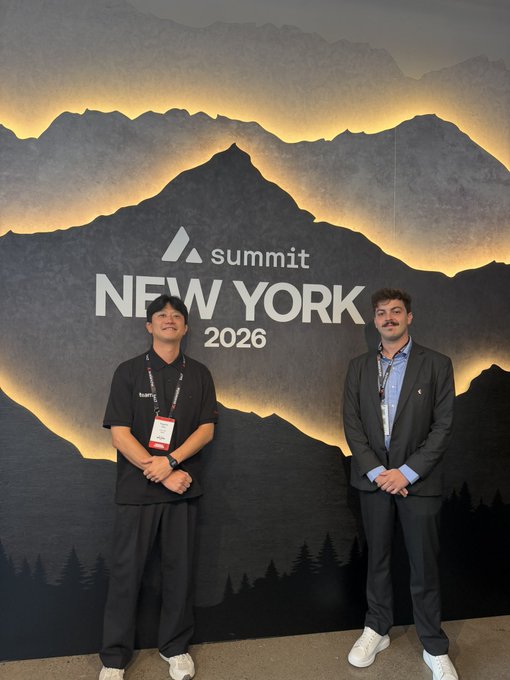 Two men pose in front of a backdrop reading 'summit NEW YORK 2026' with mountain graphics, one wearing a staff lanyard.