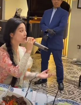 A woman with long dark hair in a floral blouse drinks from a small cup at an elegant dinner setting, while a man in a blue suit and gloves stands behind her. The image appears to relate to the post's claim about Fan Bingbing, though no text or identifying information is visible in the scene to confirm the connection.