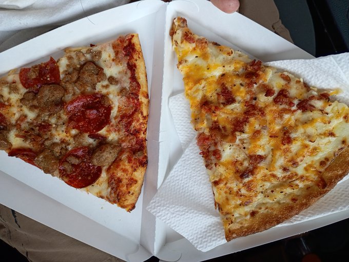 Two large slices of pizza in a white takeout box: one topped with pepperoni and sausage, and the other a plain cheese slice.