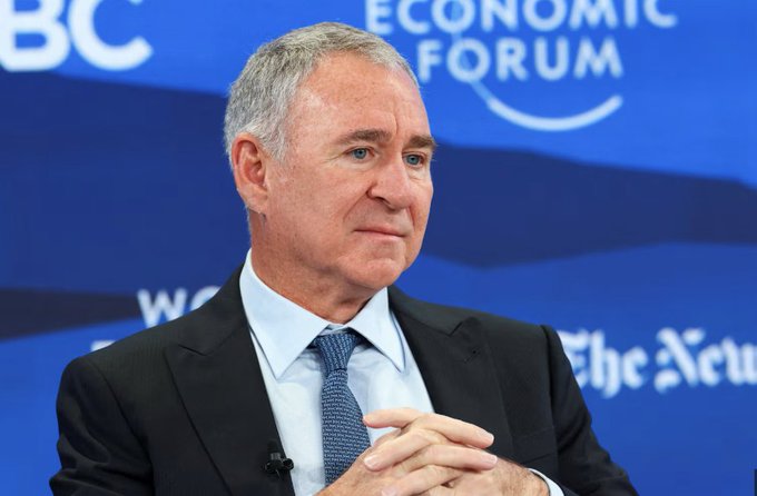 A man in a dark suit and blue tie speaking at the World Economic Forum, with 'BC', 'ECONOMIC FORUM', and 'The New' visible on the blue backdrop.