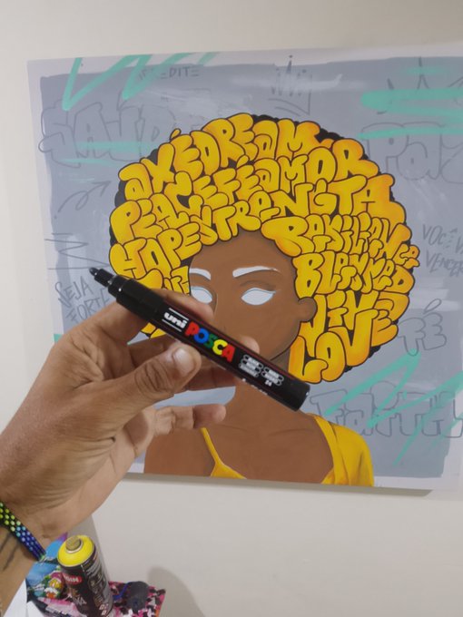 A hand holds a Uni POSCA marker in front of a vibrant artwork depicting a woman with an afro made of yellow bubble letters spelling words like "DREAMS," "PASSION," "STRENGTH," and "LOVE" against a graffiti-style background. The caption "Good morning" pairs nicely with the uplifting, motivational artwork suggesting a positive start to the day.