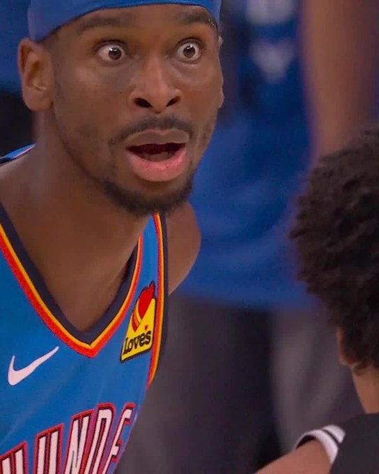 The image shows two basketball players, one wearing a blue Thunder jersey and the other wearing a black shirt. The player in the blue jersey appears surprised or shocked by something happening during the game, while the player in the black shirt looks on with interest.