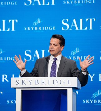 The image features a man standing at a podium, giving a speech or presentation. The background behind him has a blue wall with white text that says "Skybridge" and "Salt". There are also other words written on this wall, such as "Bitcoin will start to rally from the fourth quarter of 202 into early 203  - SkyBridge' Anthony Scaramucci", which suggests that there might be some connection between Bitcoin and the event taking place. The man is wearing a suit and tie, indicating a formal setting for his speech or presentation.