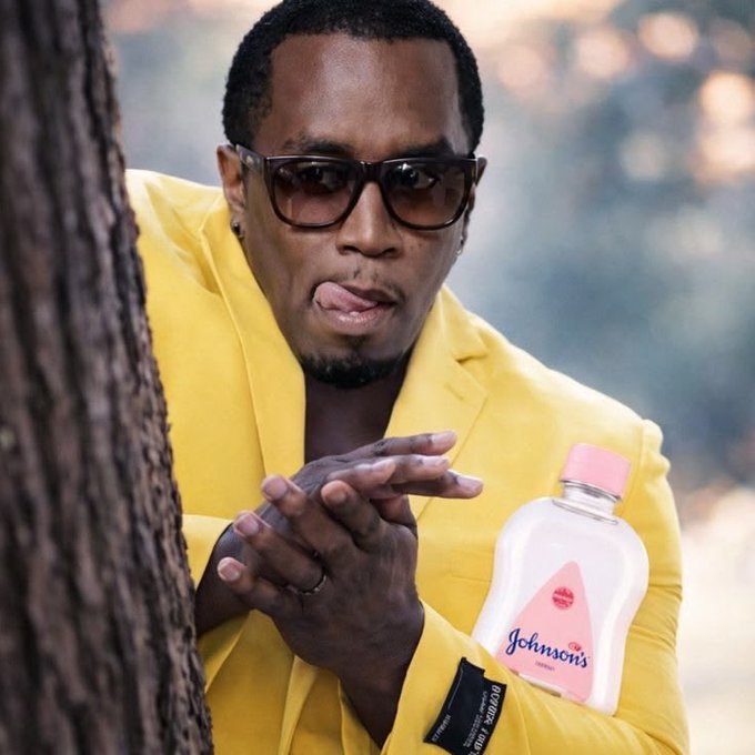 The image features a man wearing a yellow jacket, sunglasses, and a ring on his finger. He has his tongue sticking out and appears to be making a funny face or gesture for the camera. The background of the photo shows a tree trunk, suggesting that they are in an outdoor setting. There is also a bottle with the word "Johnson's" written on it next to the man.