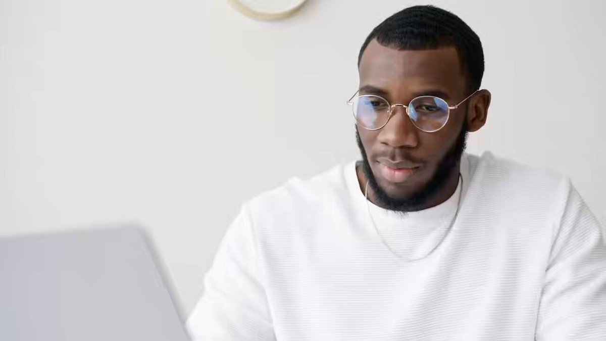 The image shows a man wearing glasses sitting at a desk with a laptop computer open in front of him. The background appears to be a white wall, which contrasts with the man's dark hair. The text "Ethereum Classic stays true to Proof-of-Work, offering strong security and real censorship resistance." is visible on this part of the image. This suggests that the man might be interested in or discussing the blockchain technology behind Ethereum Classic.