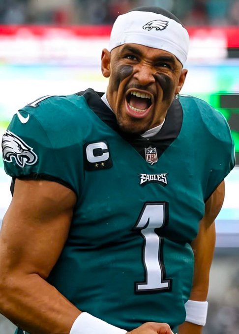 A close-up photo of Philadelphia Eagles quarterback Jalen Hurts wearing his #1 green jersey with a captain's 'C' patch, smiling broadly with black eye black under his eyes.