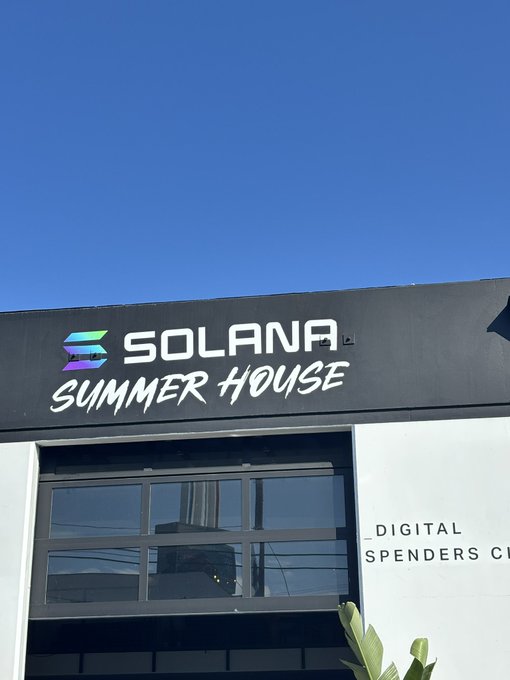 A building facade displays the Solana logo and text 'SOLANA SUMMER HOUSE' with 'DIGITAL SPENDERS C[...]' partially visible below, under a clear blue sky.