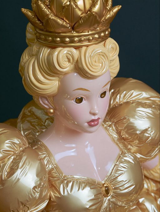 Glossy figurine of a blonde princess wearing a golden crown and elaborate golden dress, resembling a stylized Disney character.