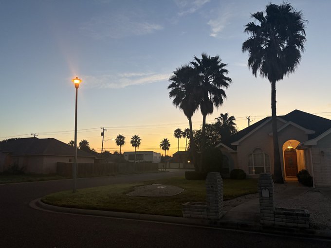 A serene twilight scene of a suburban street lined with palm trees and houses, with a glowing streetlamp under a blue and orange sunset sky.