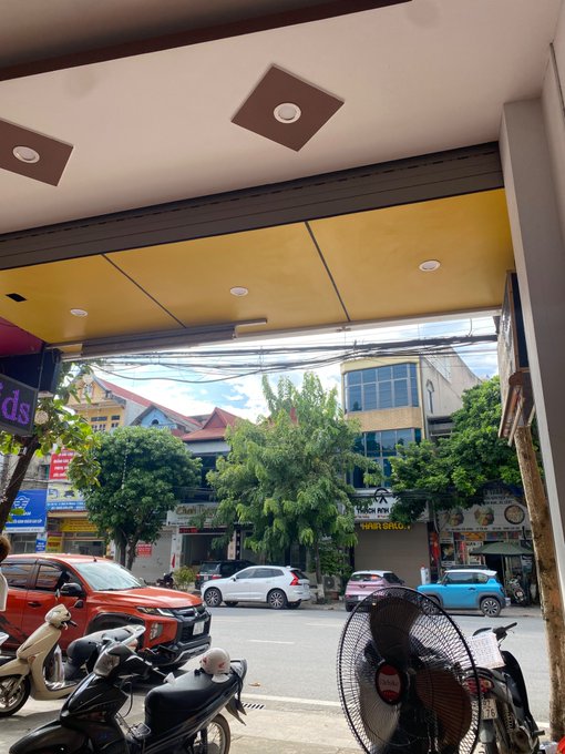 A street-level view from inside a shop or café looking out at a Vietnamese roadside scene, with motorbikes parked in the foreground (including one with a "TOYOTA" fan sign), cars passing by, and storefronts visible across the street under a yellow awning—likely taken as a casual break while reflecting on the post's guide about quitting futures trading.