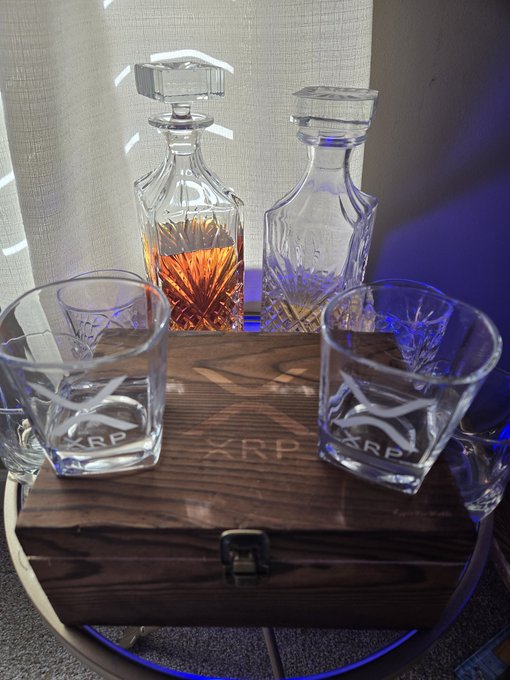 A wooden-glass decanter set and six glasses engraved with the 'XRP' logo arranged on a wooden box, with two decanters styled like XRP coins.