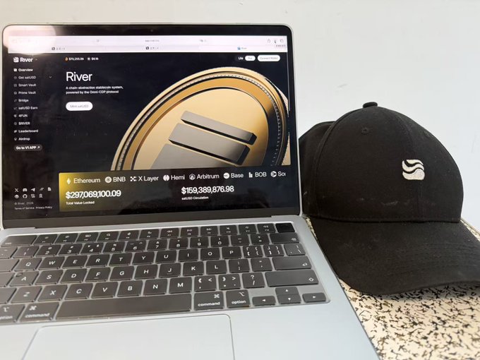 The image features an open laptop computer with a black cap placed nearby. The laptop screen displays a webpage showcasing a coin called "River" for $6.10, which appears to be a gaming currency. A white sticker also adorns the cap, adding a unique detail. At least one other post on this website has been mentioned, but it does not focus on "S5 will end on June 30th You can earn Riverpts by participating in events, staking $RIVER tokens, or even staking stablecoins!". The caption of the image seems to be a description of an event related to the Coin.